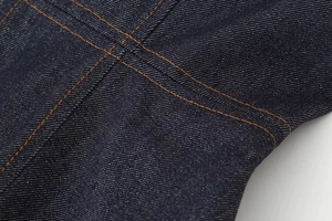Detalle de tela vaquera de sarga azul marino de alta densidad con costuras naranjas clásicas