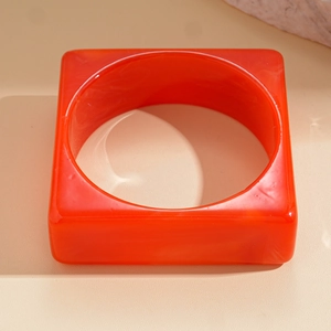 Macro shot of red acrylic resin bangle featuring bold square geometric shape and marble texture