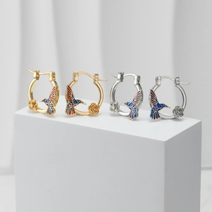 Detail of colorful enamel hummingbird and rose earrings on white geometric stands