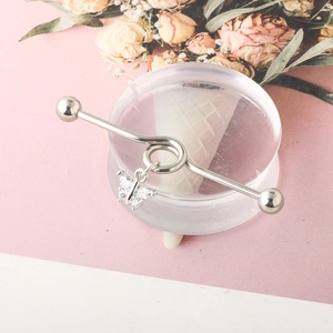 Close-up of a silver industrial barbell featuring a delicate butterfly charm with zircons