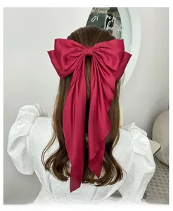 Detail view of a large red satin bow hair clip with long ribbons on wavy brown hair