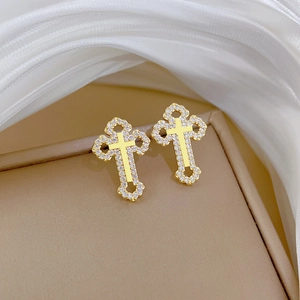 Close-up of gold titanium steel hollow cross earrings with zircon crystals on beige texture
