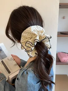 Detail of a large white and black polka dot scrunchie with elegant black piped edges