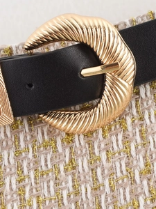 Close-up of golden spiral buckle on black belt with tweed fabric background detail
