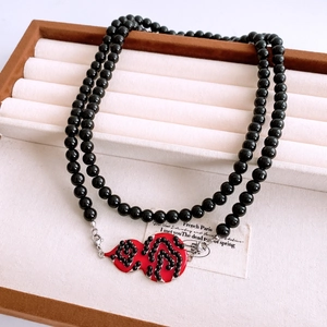 Close-up of double-layer black beaded necklace with red gourd pendant on jewelry tray