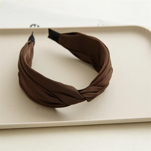 Close-up of a brown knotted headband with elegant silk texture on a minimalist tray