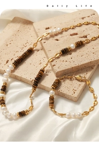 Detail of tiger eye and pearl jewelry set with gold coffee bean chain on stone