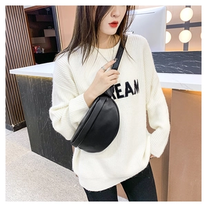 Close-up of stylish black leather crossbody chest bag worn over a casual knit sweater