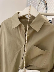Gros plan de la texture de la chemise kaki avec bandoulière dorée sur cintre blanc