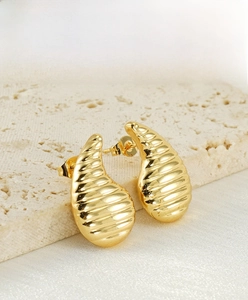 Détail macro de boucles d'oreilles goutte dorées avec rainures ondulées sur pierre
