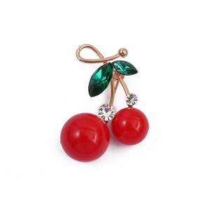 Elegant red cherry brooch with green leaf gems and gold metal stems on white background