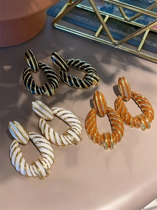 Detailed view of striped enamel spiral drop earrings in black white and orange gold tones