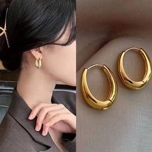 Polished gold thick hoop earrings in water-drop design shown on model and silk background