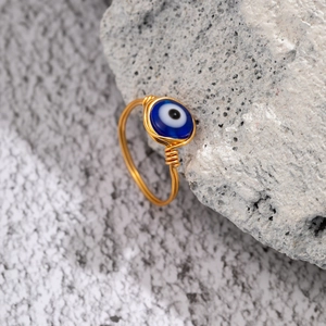 Handmade gold wire wrapped ring featuring a dark blue opal evil eye bead on a natural stone