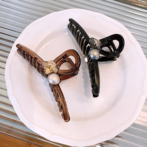 Elegant pearl bow hair claws in amber and black resin displayed on a ceramic tray