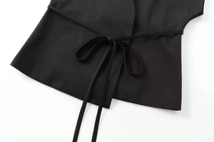 Détail du gilet noir sans manches élégant montrant la taille nouée et le tissu texturé
