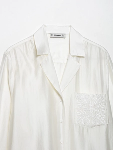 Detailed view of white linen blend shirt with an embroidered pocket and satin texture