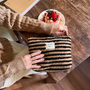 Detail of plush striped makeup bag with textile label on dark wood tabletop