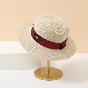 Detail of straw boater hat with burgundy ribbon and gold hardware on a display stand