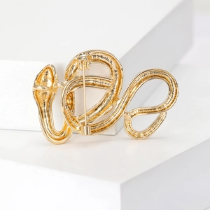 Elegant gold snake brooch with vintage design on minimalist white display stand