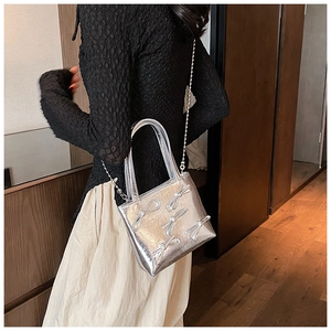 Detail shot of silver glossy handbag featuring 3D bows and a delicate metal chain strap