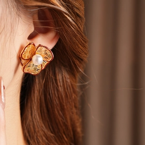 Close-up of a gold-plated flower earring with mesh texture and a central pearl detail