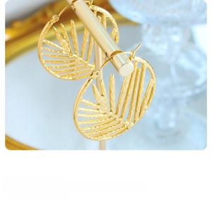 Detailed close-up of 18K gold palm leaf hollow hoop earrings on a luxury display stand