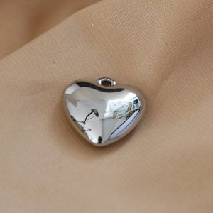 Close-up of polished heart-shaped metal pendant with reflective surface on soft fabric