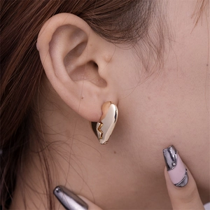 Detail view of gold irregular broken heart earrings with mirror polished finish on model
