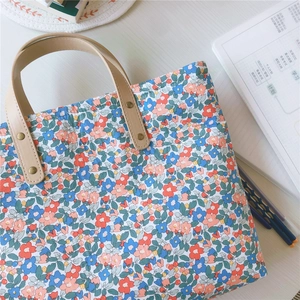 Dettaglio della borsa floreale con manici in pelle marrone e rivetti metallici
