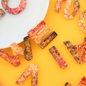 Creative resin alphabet keychain with gold foil flakes and vibrant orange tones