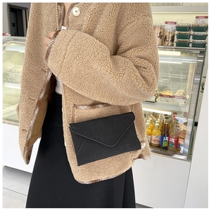 Close-up of a black suede envelope bag with a metal chain strap worn on the shoulder
