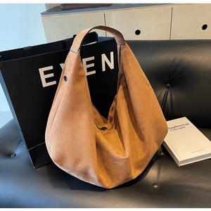 Detail of a large hobo bag in brown matte suede finish placed on a black leather sofa