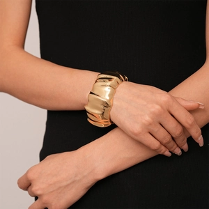 Golden wide cuff bracelet with pleated metal texture on female wrist with black background