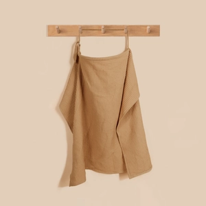 Caramel waffle weave cotton breastfeeding cover on wooden rack in minimalist style