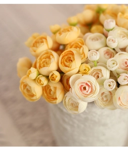 Close-up of yellow and cream artificial camellia silk flowers in a white ceramic vase