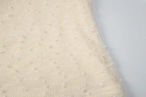 Close-up of cream knit fabric with 3D dot embroidery and delicate breathable texture