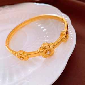 Détail d'un bracelet fleuri doré orné de zircons posé dans un plat décoratif en céramique