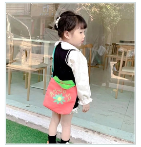 Kid's red canvas crossbody bag with flower print and green straps shown on a model