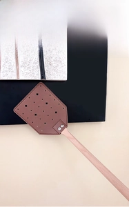 Detail of leather flyswatter with floral cutout pattern and sturdy long wooden handle