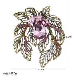 Detailed view of a vintage gold-toned leaf brooch with pink gems and colorful rhinestones