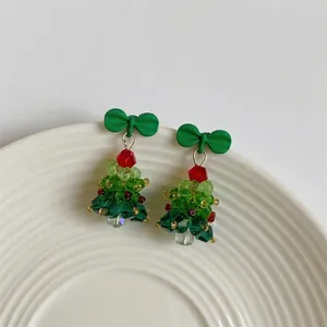 Detailed shot of beaded crystal Christmas tree earrings with a red bow on a white plate