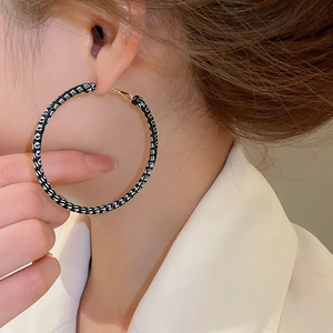 Détail de grandes créoles dorées avec motif de lettres noir et blanc sur modèle