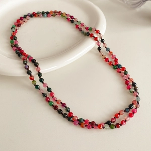 Detail of bohemian long necklace featuring multi-colored stone beads on a white surface