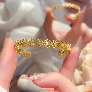 Close-up of golden open cuff bracelet featuring an intricate hollow daisy floral pattern