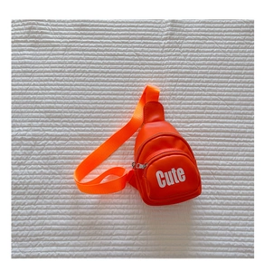 Close-up of bright orange PU leather chest bag for kids with white Cute lettering detail