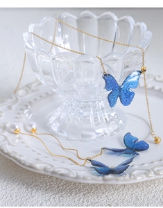 Details von Schmetterling-Halskette und Perlenohrringen auf einem weißen Keramiktablett