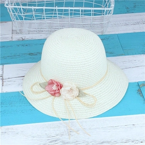 Détail d'un chapeau de paille crème orné de fleurs en tissu et d'un nœud en corde