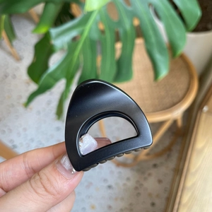 Detailed view of matte black triangular shark clip held against a natural background