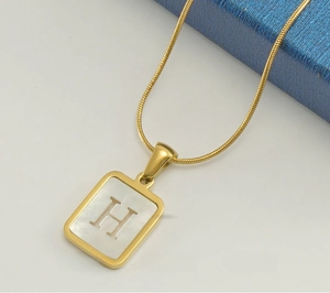 Macro detail of 18K gold stainless steel H letter pendant with white shell inlay